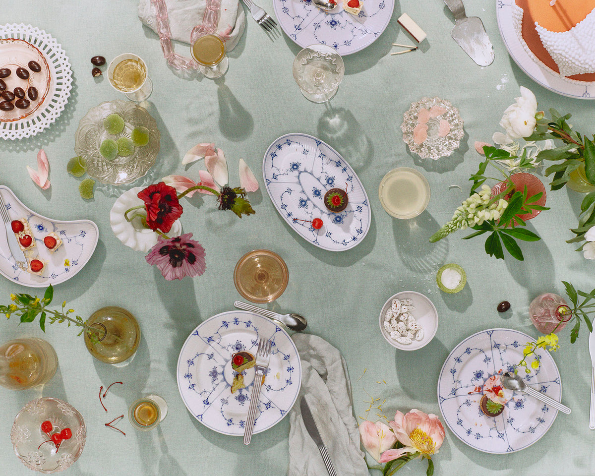 A light green table seen from above with Blue Fluted Plain porcelain plates, glasses, and flowers throughout the table.