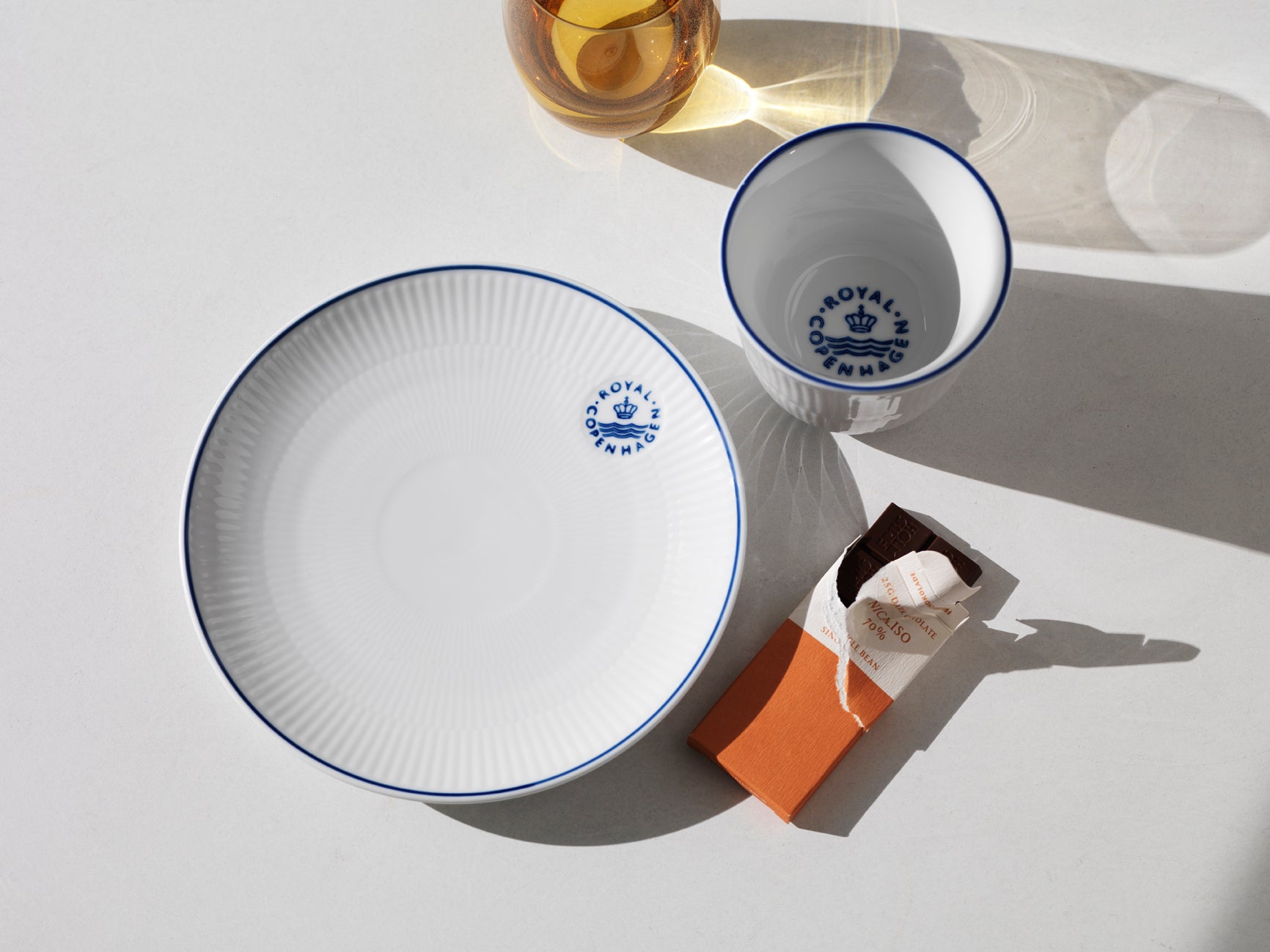 Ceramic plate and cup with blue rim and 'Royal Copenhagen' logo on a light gray background