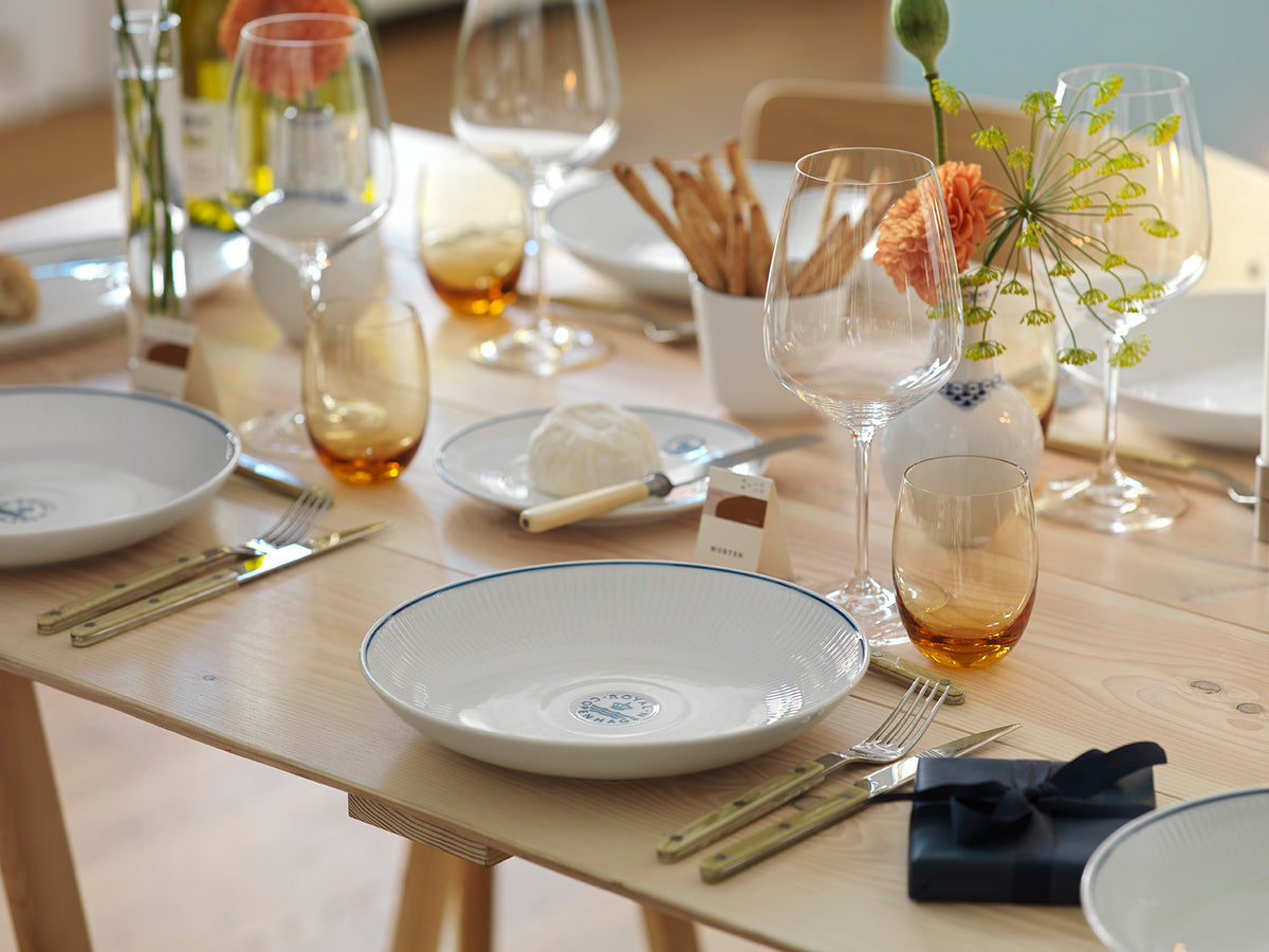 Dining table set with Blueline plates, glasses, and cutlery on a wooden surface.