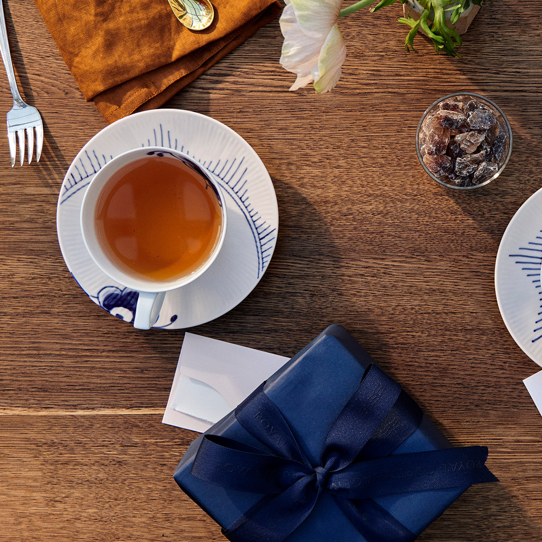 Blue Fluted Mega Tea cup on a saucer with a wrapped gift and card on a wooden table