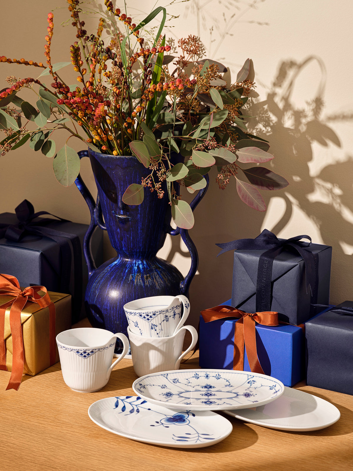 Decorative table setting with blue and white crockery, a blue vase, and wrapped gifts.
