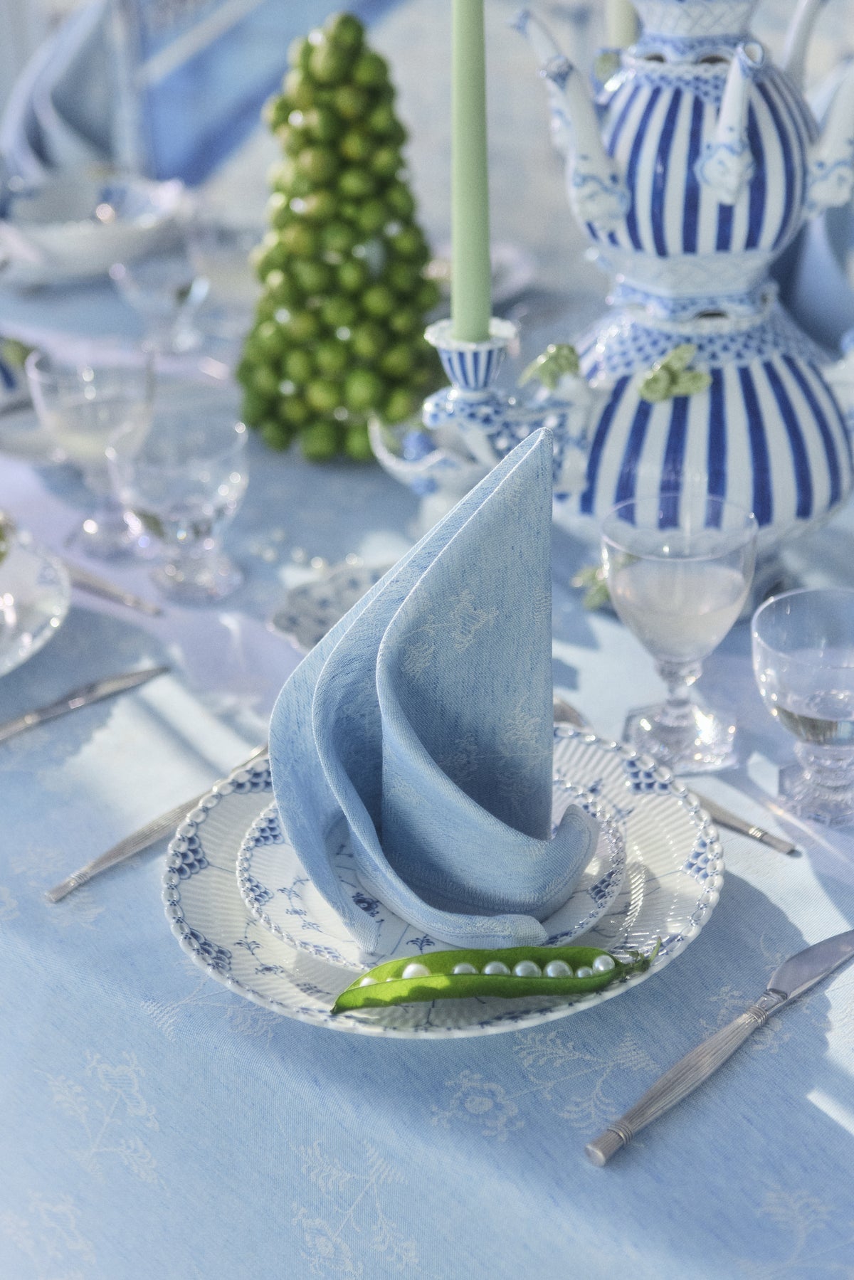 A close-up f a table setting focusing on the Heritage napkin in light blue which is placed on top of two stacked Fluted Half Lace and Blue Fluted Full Lace plates.