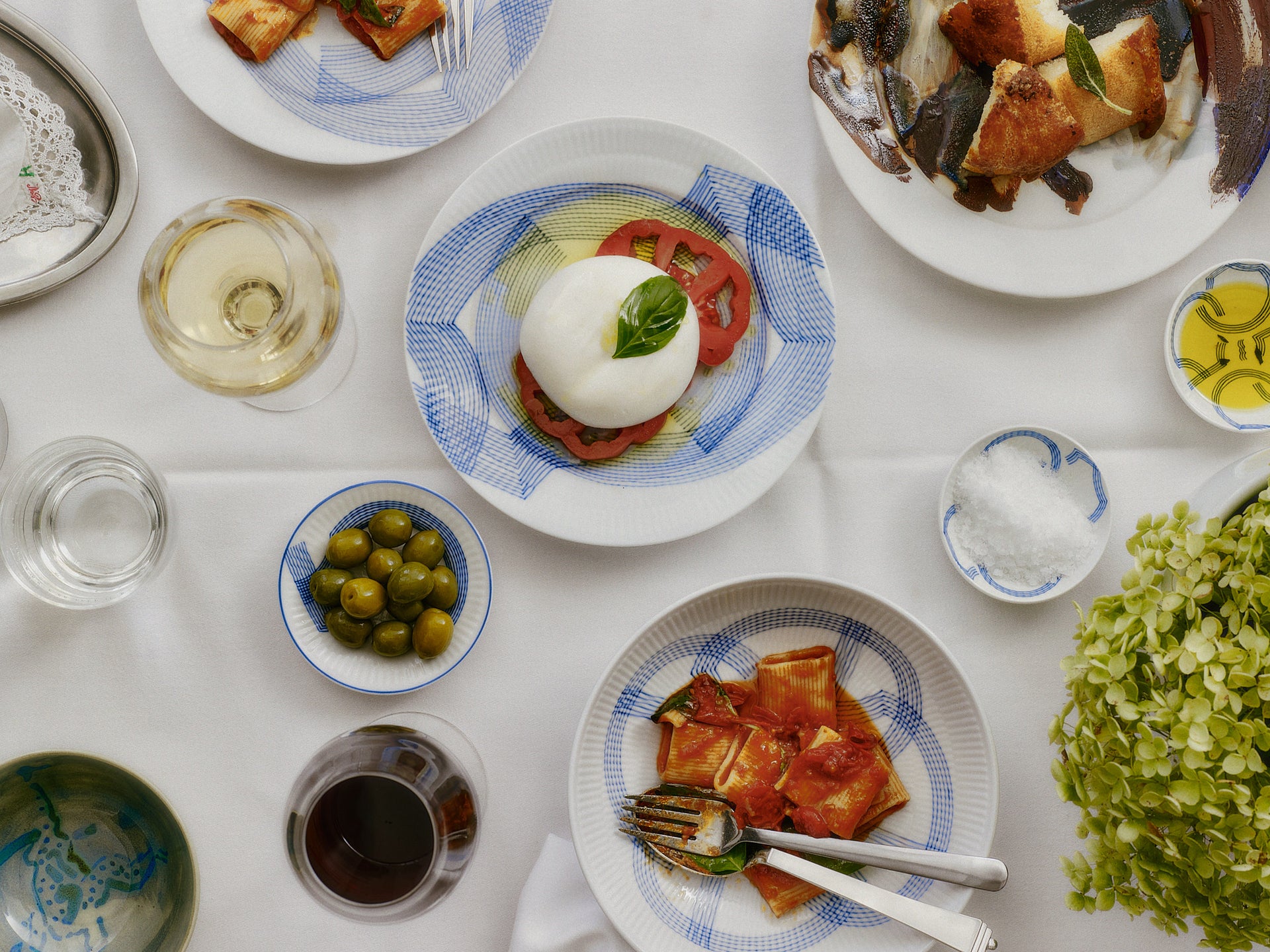 Table set with Motif with Italian dishes including pizza, mozzarella, and olives on a white tablecloth.
