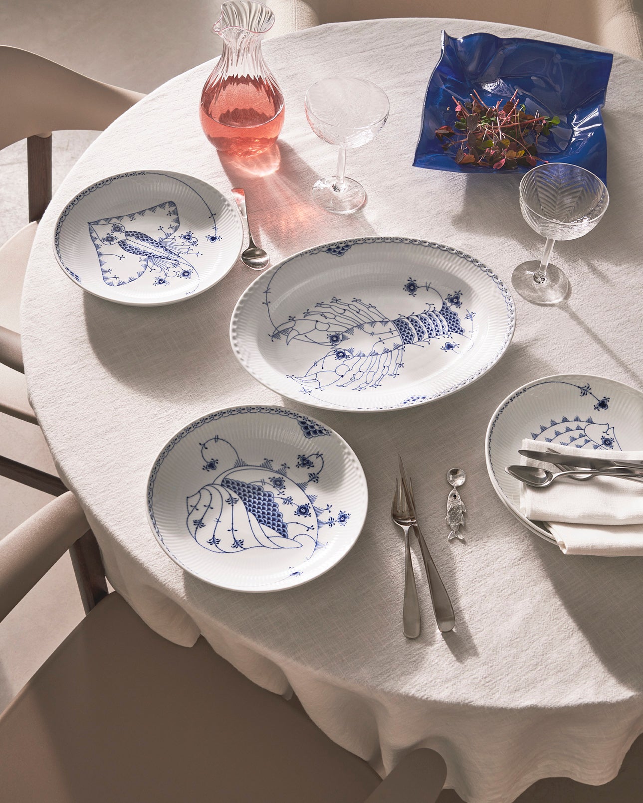Dining table set with plates from Royal Creature, glasses, and cutlery on a white tablecloth.