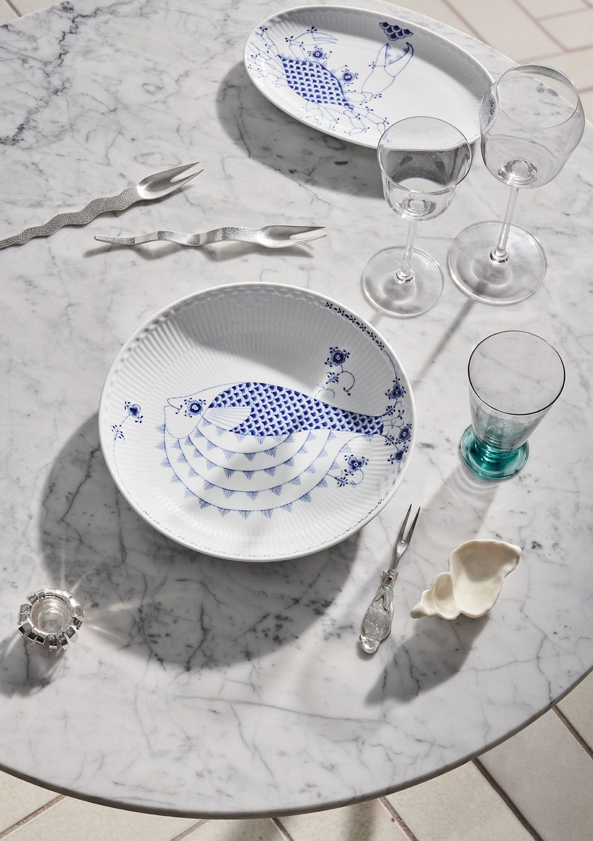 Dining table setting with Royal Creatures plates, glasses, and cutlery on a marble surface.