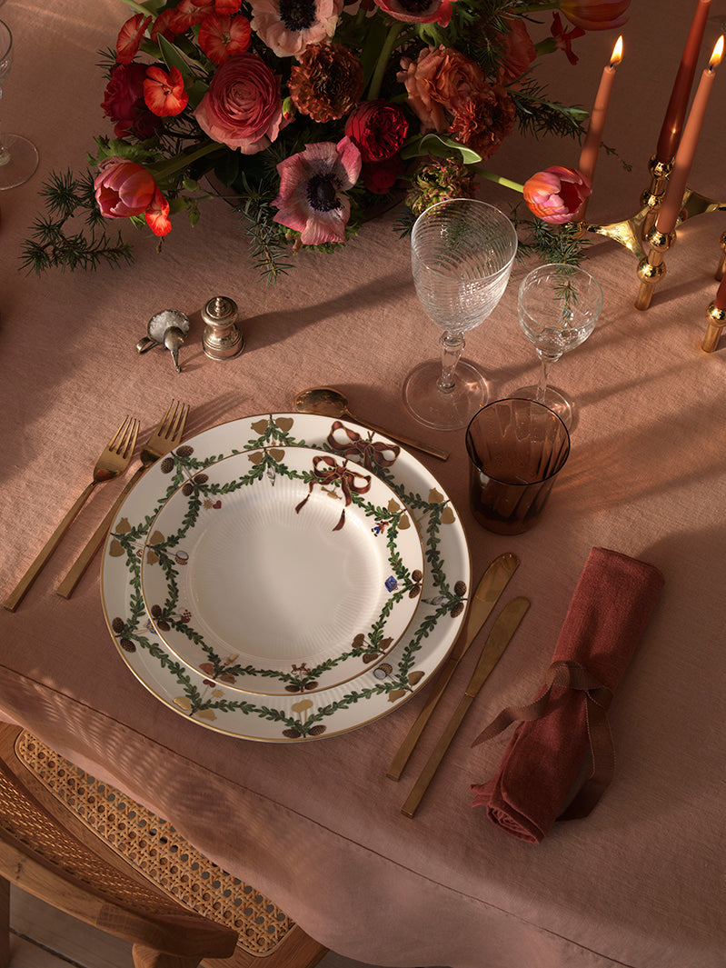 Elegant Christmas table setting with floral arrangement, candles, and decorative Star Fluted Christmas plates from Royal Copenhagen.