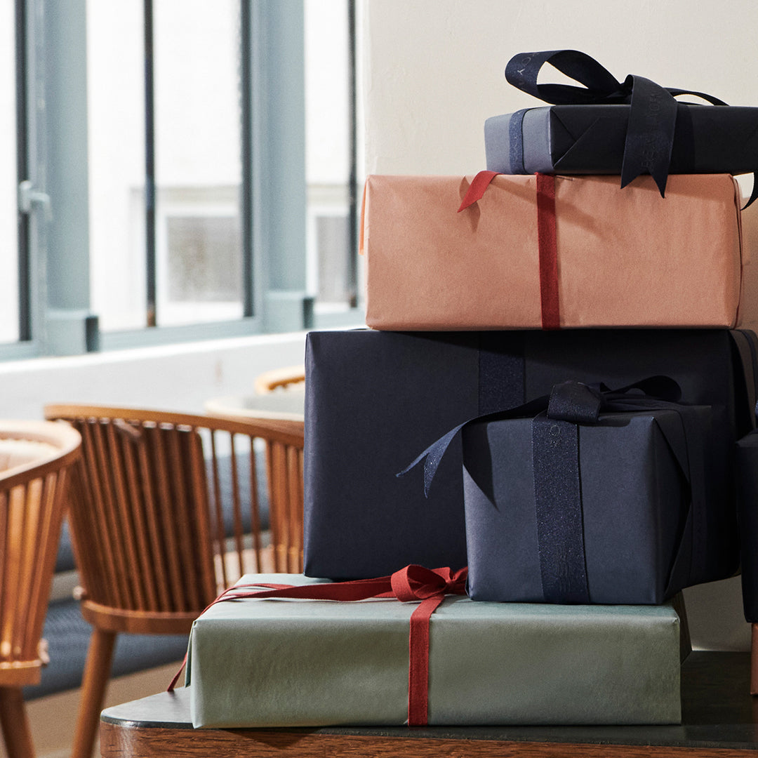 Stack of wrapped gifts with ribbons on a table in a room with large windows.