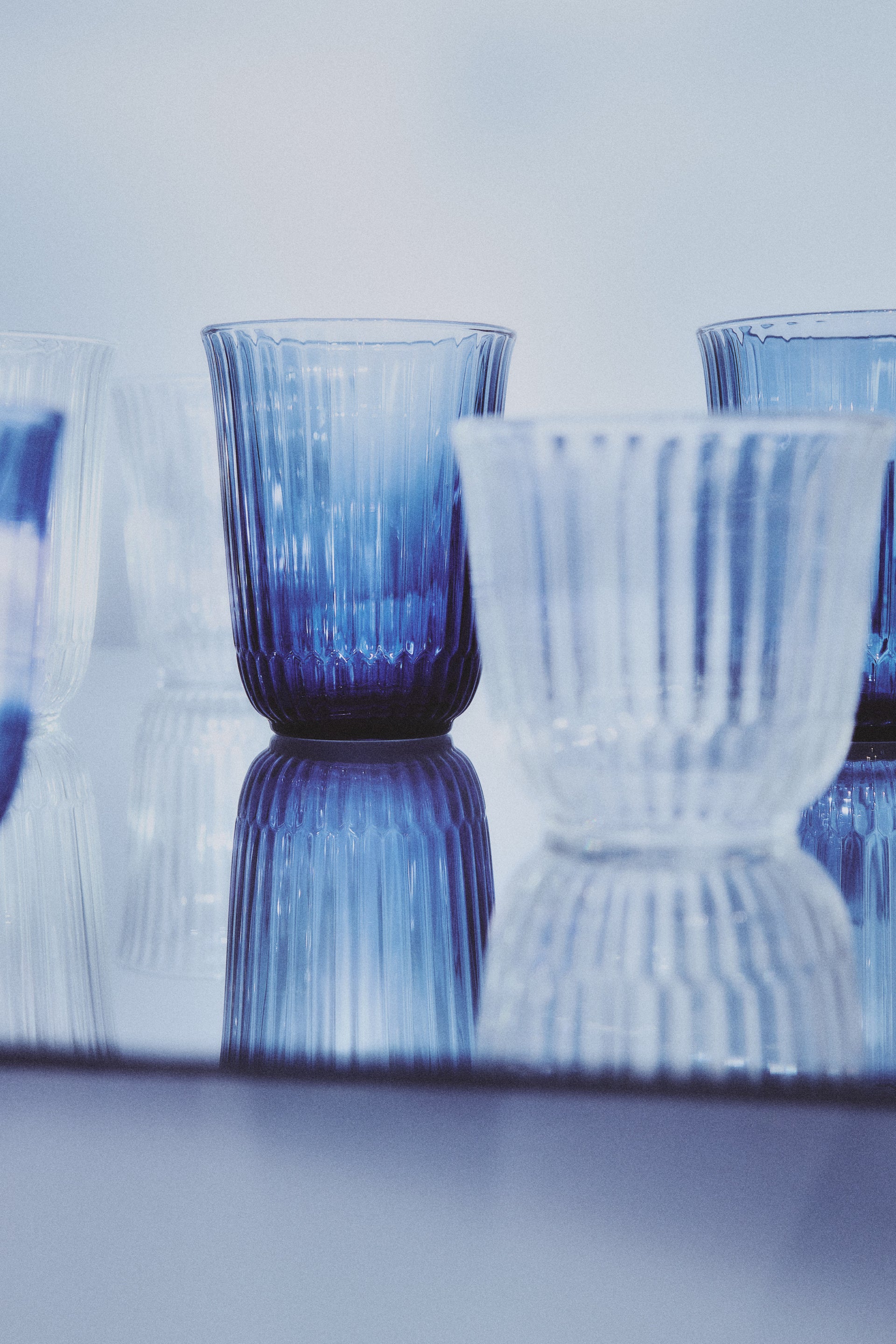 Set of Waves Glassware in blue and clear glasses on a reflective surface with a blurred background