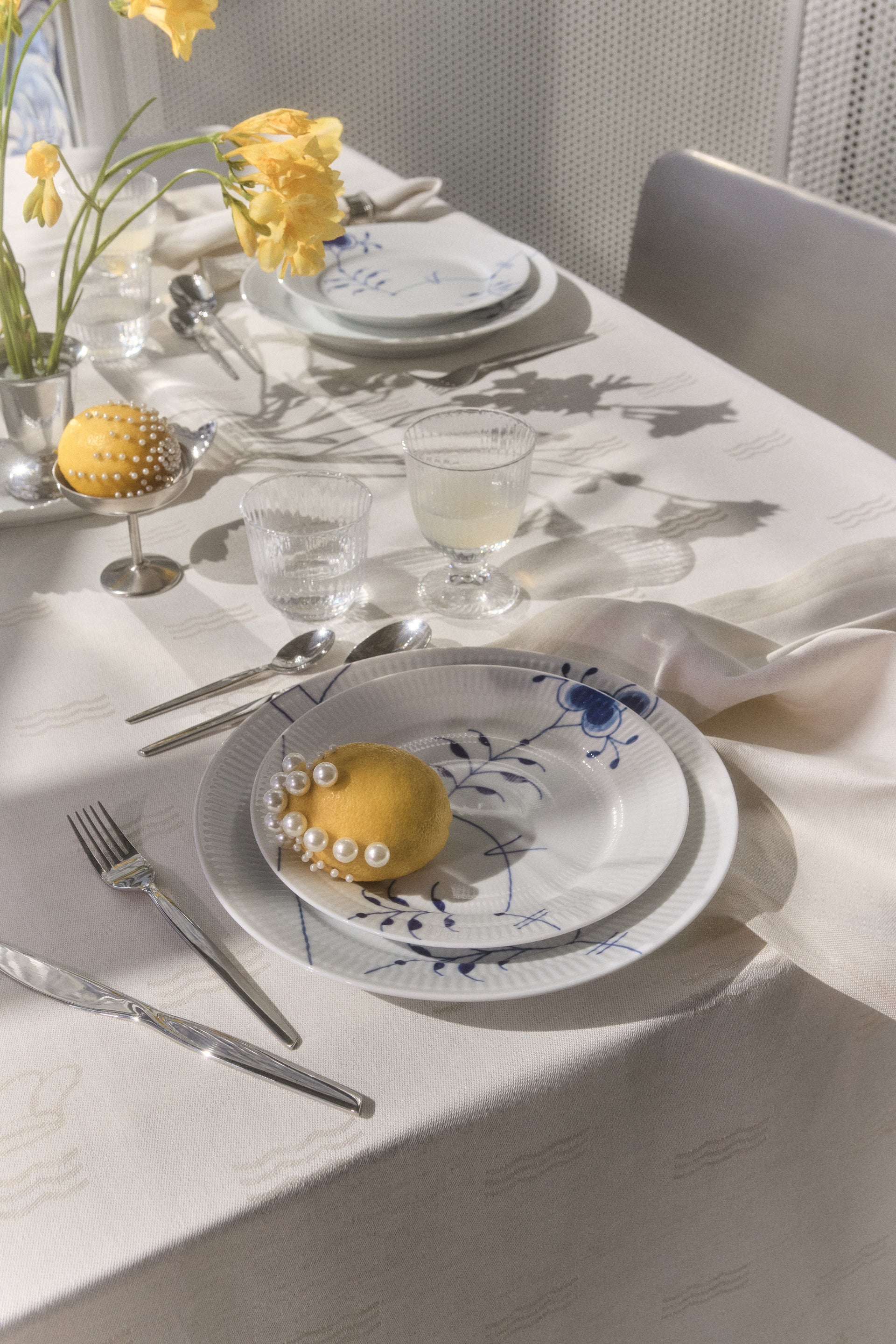 Elegant table set with Blue Fluted Mega porcelain from Royal Copenhagen and a yellow floral arrangement and lemons on an off-white Waves tablecloth.
