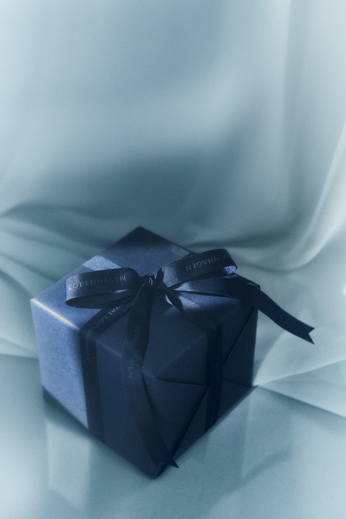 Blue gift with a blue ribbon on a white draped background